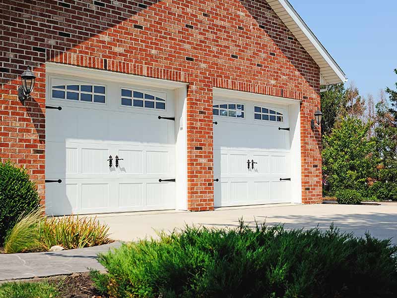 Two white carriage house style garage doors on a brick home